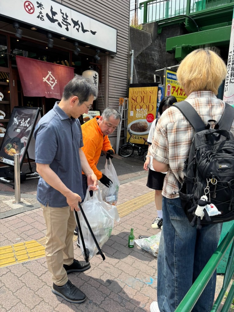 청소 활동에 참여한 자원봉사자들이 쓰레기를 수거하고 있는 모습. 배경에는 가게와 광고판이 보인다.