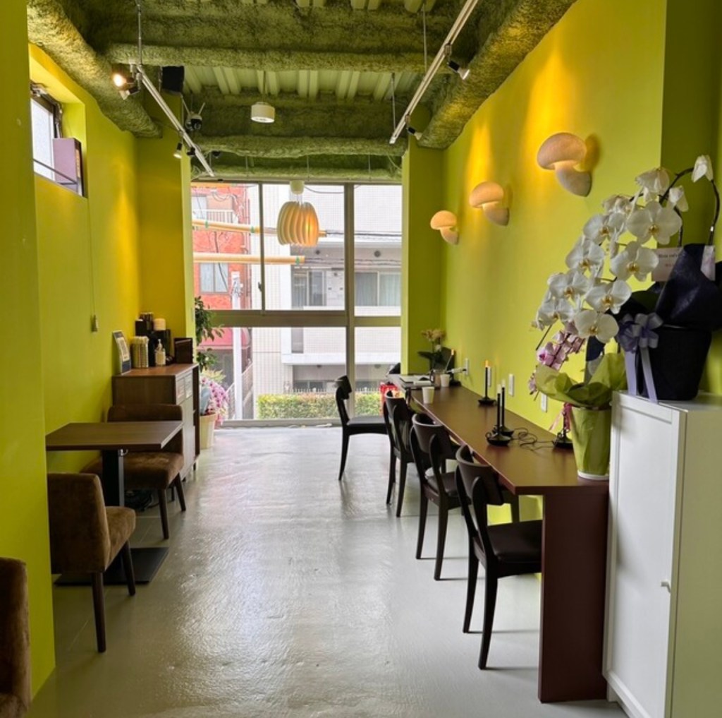 A cozy interior of the Moia Korean Cuisine Cafe & Bar, featuring bright green walls, modern lighting, and a long dining table set with chairs, creating a welcoming atmosphere for diners.