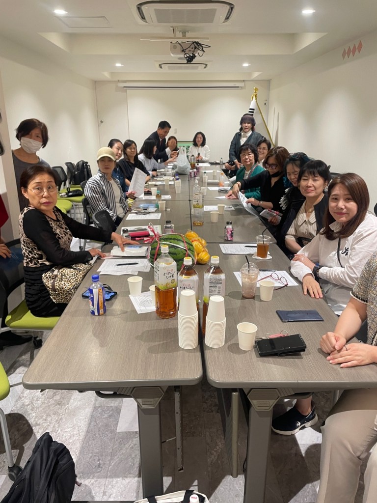 A group of people attending a monthly meeting at the 'Love Sharing' organization in a conference room, with drinks and documents on the table.