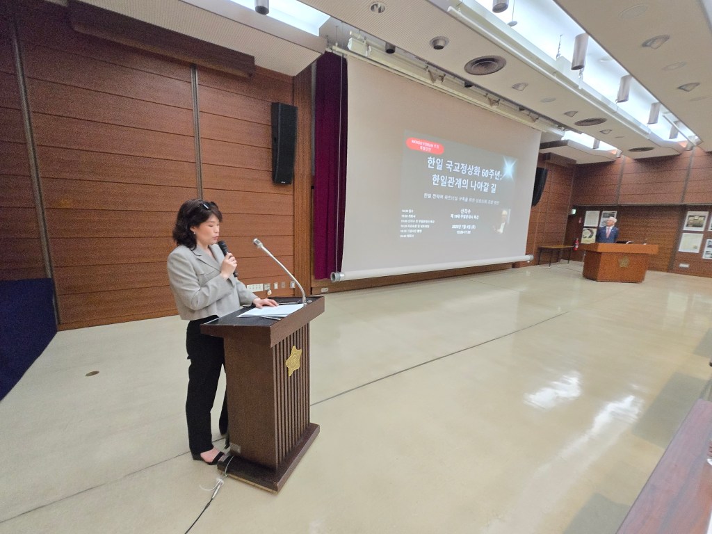 한일 국교정상화 60주년 기념 강연회에서 발언 중인 여성 발표자와 배경의 화면을 보여주는 모습.