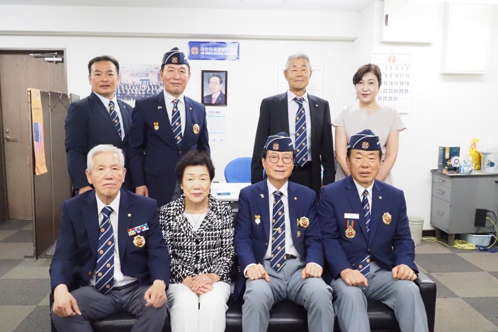 A group photo of the Japanese chapter of the Korean Veterans Association, featuring members in uniform, seated and standing together in a formal setting.
