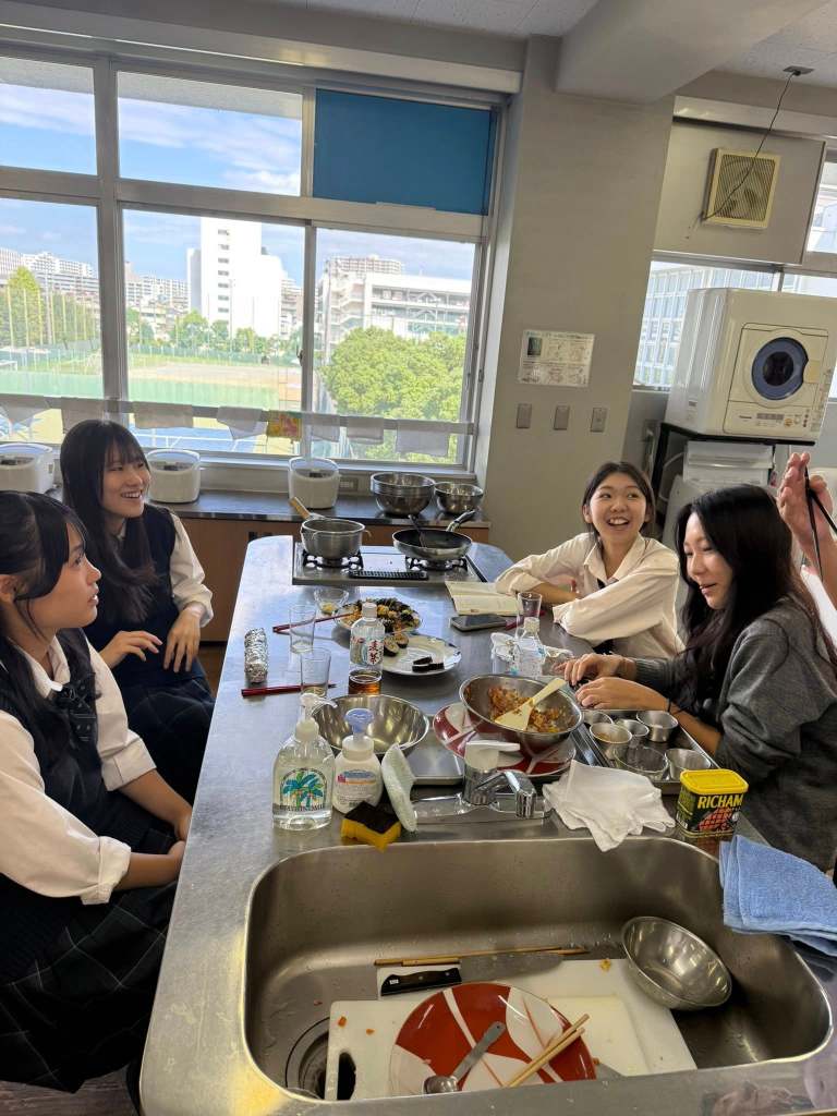 A group of students engaged in a cooking class at a high school in Tokyo, preparing kimbap with various ingredients laid out on a countertop.