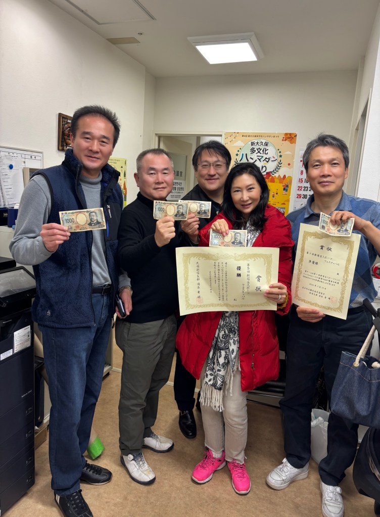일곱명의 사람들이 상장과 현금을 들고 웃고 있는 모습으로, 사무실 내부에 서 있다.